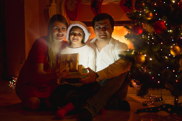 smiling family sitting at fireplace and opening Christmas gift b