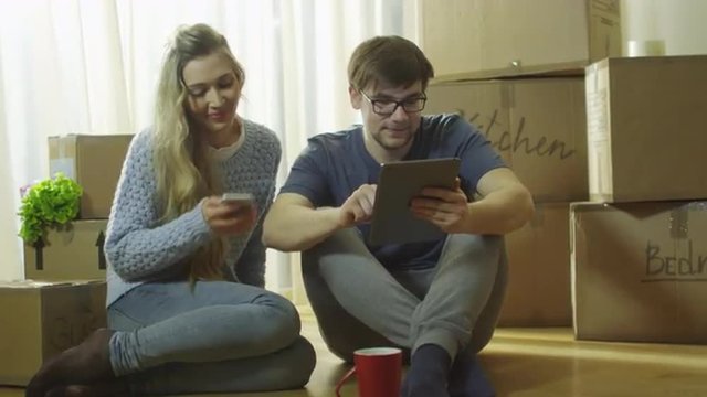 Young Couple is Using Phone and Tablet for Entertainment in New House. Shot on RED Cinema Camera in 4K (UHD).