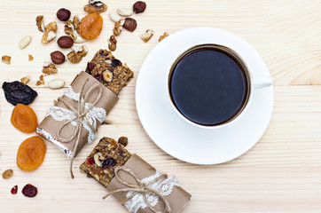 Homemade rustic granola bars with dried fruits and handmade packaged and cup of coffee on wooden background