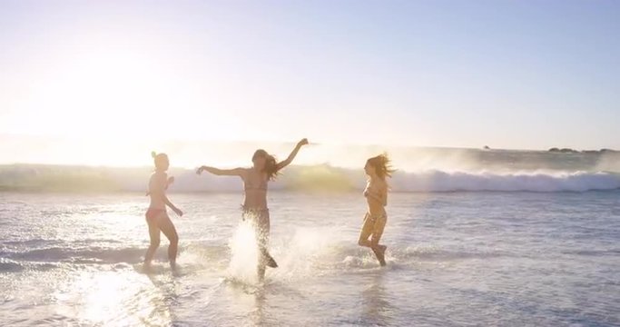 Young women splashing in waves in slow motion playing in ocean on tropical beach