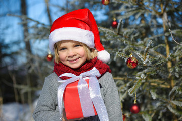 Portrait of cute little boy with christmas gift in the winter forest