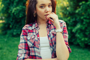 Brown hair girl sitting on the grass in the park and posing to the photo.