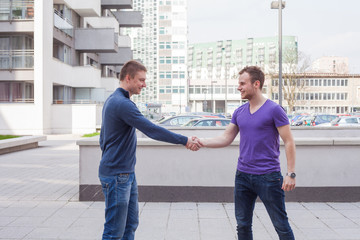 Happy young student giving a handshake to his classmate. Urban background.