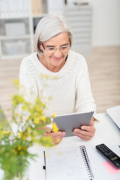 moderne seniorin sitzt am schreibtisch und schaut auf tablet-pc
