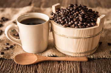 Coffee beans in wooden bowl and coffee cup on wooden background.