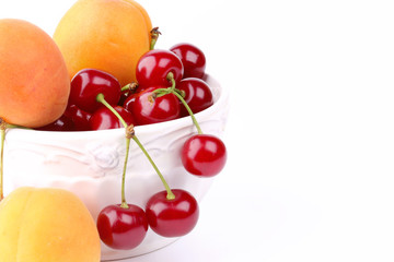 cherries and apricots in ceramic bowl isolated on white background