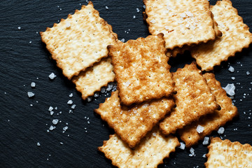 Crispy golden crackers with salt on dark stone background, top v