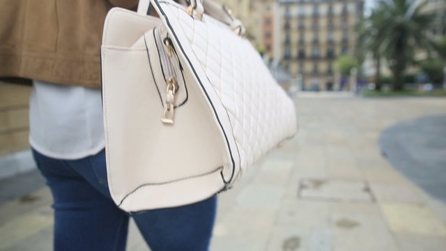 Closeup of purse eld by woman walking in city street