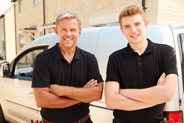 Portrait of a young and a middle aged tradesman by their van