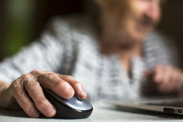 Closeup of the hand of an old woman holding a computer mouse. - Powered by Adobe