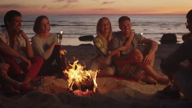 Group of Friends Sitting near Campfire at Night and Hanging Out