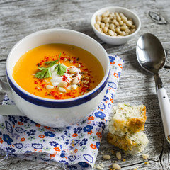 pumpkin soup in white ceramic Cup and a piece of cake with cheese and herbs on a light wooden background