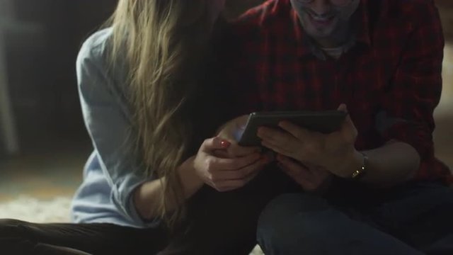 Happy Smiling Young Couple are Using Tablet PC for Entertainment at Home at Evening Time.