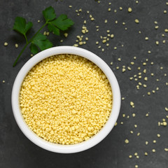 Raw couscous in small bowl, photographed overhead on slate with natural light (Selective Focus,...