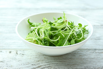 Fresh mixed green salad in bowl on wooden table close up