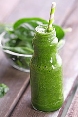 Glass bottle of spinach juice on wooden table, closeup
