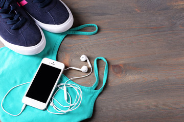 Mobile phone and earphones with t-shirt and shoes on wooden table, closeup