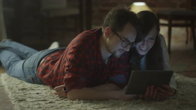 Young Happy Smiling Couple using Tablet PC for Entertainment at Home at Evening Time. Casual Lifestyle.