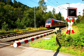 Zug nähert sich einem Bahnübergang mit geschlossener Schranke 