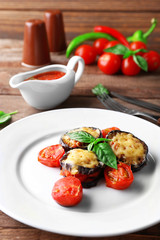 Dish of eggplant with cherry tomatoes and cheese in white plate on wooden table, closeup