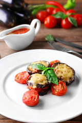 Dish of eggplant with cherry tomatoes and cheese in white plate on wooden table, closeup