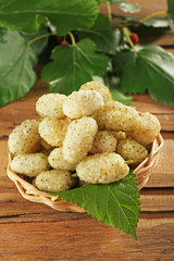 Fresh mulberry in wicker basket on wooden table, closeup