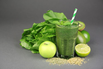 Green healthy juice with fruits and herbs on gray background