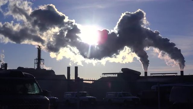Global warming is suggested by shots of a steel mill belching smoke into the air with sun background.