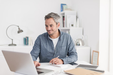 Portrait of a smiling grey hair man with beard, working at home