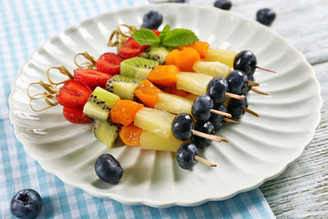 Fresh fruits on skewers in plate on table, closeup