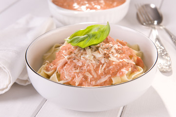 ribbons of pasta with tomato sauce and cheese in a white bowl, on white boards  