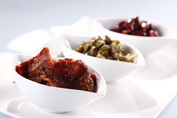 capers, tomatoes, beans in white bowls on a white background 