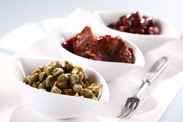capers, tomatoes, beans in white bowls on a white background 