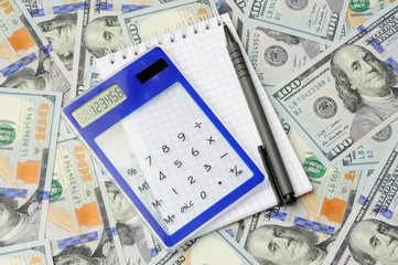 Calculator with pen and notepad on dollars background