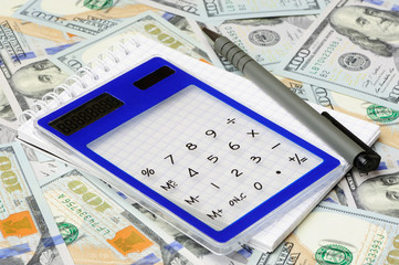 Calculator with pen and notepad on dollars background