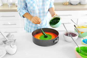 Young woman making rainbow cake in kitchen