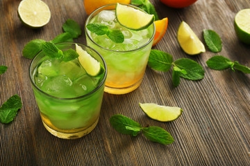 Glasses of lime juice with orange on wooden table, closeup