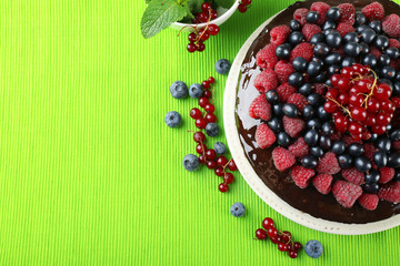 Delicious chocolate cake with summer berries on green tablecloth, closeup