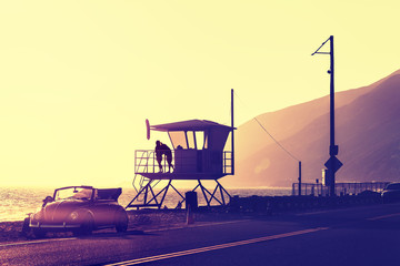 Vintage filtered sunset over beach with lifeguard tower seen from the street, California, USA.
