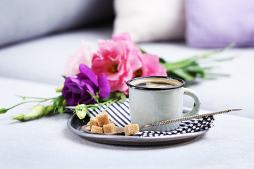 Cup of coffee with flowers on tray on sofa in room