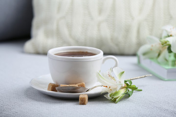 Cup of coffee with lump sugar and flowers on sofa