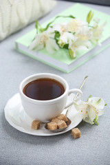 Obraz na płótnie Canvas Cup of coffee with lump sugar and flowers on sofa