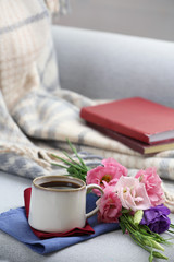 Cup of coffee with flowers near books on sofa in room