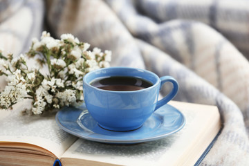Blue cup of coffee with open book on sofa in room