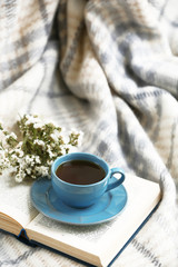Blue cup of coffee with open book on sofa in room