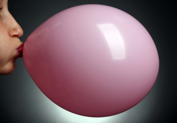 Young woman inflating balloon on gray background