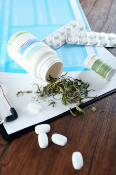 Bottle of dry medical cannabis and pills with clipboard on table close up