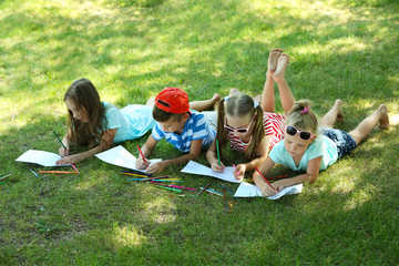 Happy active children lying on green grass and drawing in park