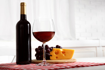 Red grape and cheese with glass bottle of wine on light interior background