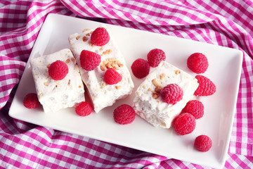 Sweet nougat with nuts and raspberries on plate close up